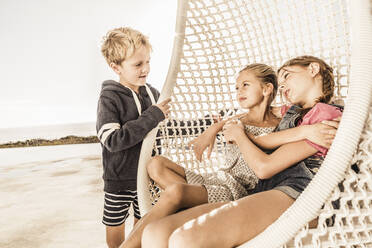 Two girls hugging in hanging chair looking at boy - SDAHF00130