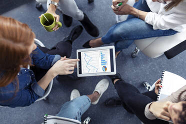 Geschäftsfrauen verwenden Diagramme auf einem digitalen Tablet während einer Besprechung in einem Büro - JSRF00841