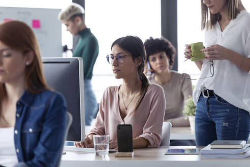 Geschäftsfrau arbeitet am Computer in einem Büro, der Chef steht neben ihr - JSRF00845