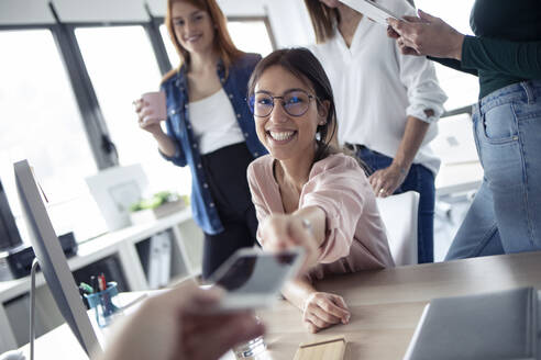 Smiling businesswoman giving a smartphone to her colleague - JSRF00850