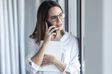 Female entrepreneur phoning and looking out of the window in office - JSRF00869