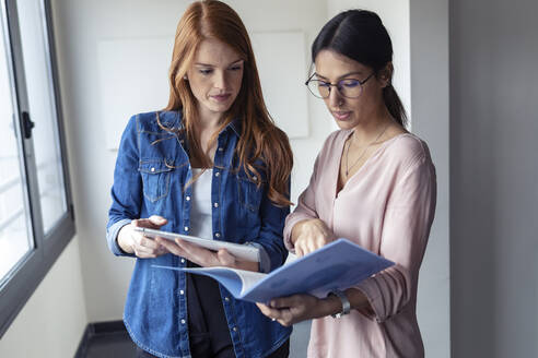 Geschäftsfrauen, die im Büro ein digitales Tablet benutzen und Dokumente ansehen - JSRF00889