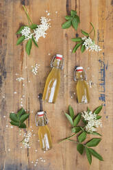 Holunderblüten (Sambucus) mit Blättern und Holunderblütensirupflaschen auf einem Holztisch - GWF06429