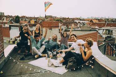 Happy male and female friends cheering on terrace while enjoying rooftop party in city - MASF16650