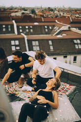 High angle view of male and female friends talking while relaxing on terrace during party - MASF16655