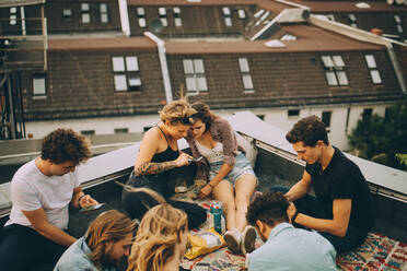 Male and female friends using smart phones while sitting on terrace during party - MASF16660