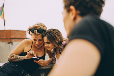 Weibliche Freunde schauen auf ihr Handy, während sie sich auf einer Party vergnügen - MASF16662