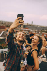 Glücklicher Mann, der ein Selfie mit fröhlichen Freunden während einer Dachparty auf der Terrasse macht - MASF16677
