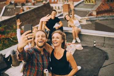 Fröhlicher Mann, der ein Selfie mit Freunden auf seinem Smartphone macht, während er eine Party auf der Terrasse genießt - MASF16678