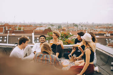 Friends enjoying beer while sitting together on terrace at rooftop party - MASF16685