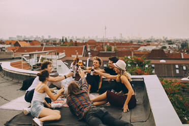 Cheerful friends toasting beer while relaxing on terrace at city - MASF16687