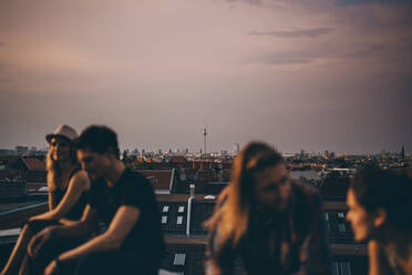 Freunde unterhalten sich auf der Terrasse während einer Dachparty in der Stadt in der Abenddämmerung - MASF16689