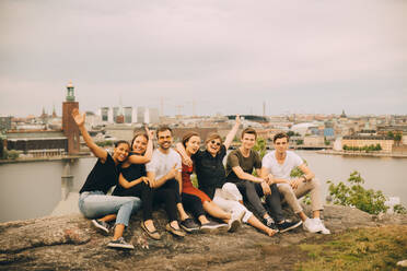 Portrait of happy friends sitting on rock formation against sky - MASF16705