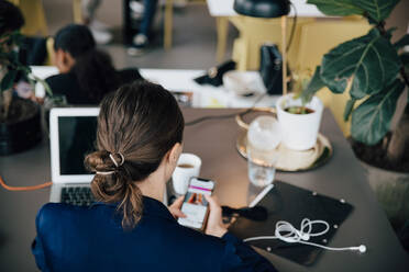 Rückansicht einer Geschäftsfrau, die einen Laptop und ein Mobiltelefon benutzt, während sie an einem Bürotisch sitzt - MASF16731