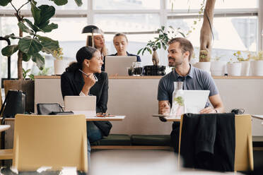 Männliche und weibliche Kollegen unterhalten sich bei der Arbeit am Schreibtisch im Coworking Space - MASF16734