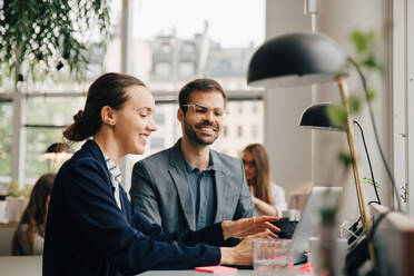 Male and female business colleagues discussing over laptop at desk in creative office - MASF16737