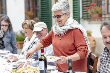 Frau serviert Nudeln beim Familienessen im Garten, Florenz, Italien - CUF54747