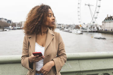 Junge Frau mit Mobiltelefon in der Stadt und Lonon Eye im Hintergrund, London, UK - WPEF02548