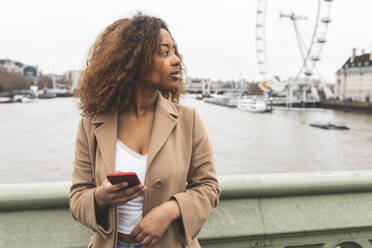 Young woman with cell phone in the city and Lonon Eye in background, London, UK - WPEF02548