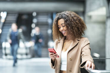 Lächelnde junge Frau, die in einer U-Bahn-Station ein Handy benutzt - WPEF02560