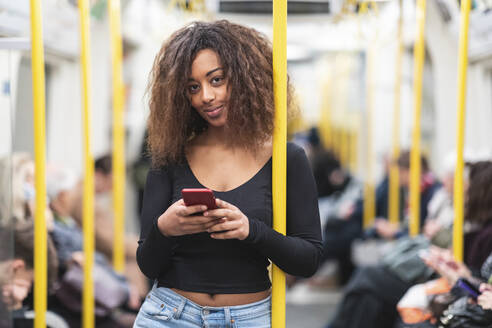 Porträt einer lächelnden jungen Frau mit Smartphone in einer U-Bahn - WPEF02568
