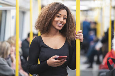 Porträt einer lächelnden jungen Frau mit Smartphone in einer U-Bahn - WPEF02569