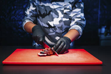 Chef preparing a dish in restaurant kitchen cutting meat - DGOF00340