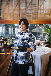 Portrait of smiling woman serving a dish in restaurant - DGOF00373