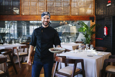 Porträt eines lächelnden Mannes, der ein Gericht im Restaurant serviert - DGOF00377