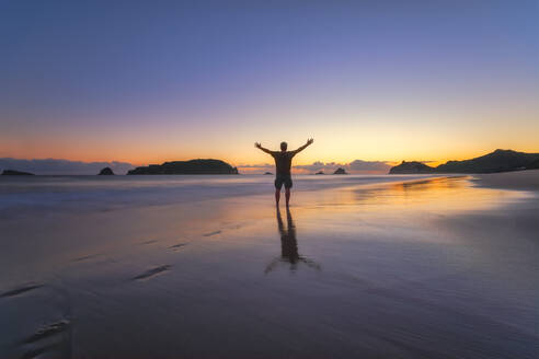 Mann mit erhobenen Armen am Hahei Beach bei Sonnenuntergang, Waikato, Nordinsel, Neuseeland - SMAF01833