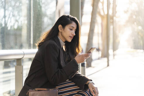 Junge Frau mit Smartphone an der Straßenbahnhaltestelle - AFVF05288
