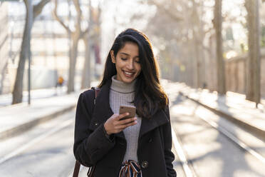 Lächelnde junge Frau mit Smartphone in einer Straßenbahnlinie - AFVF05299