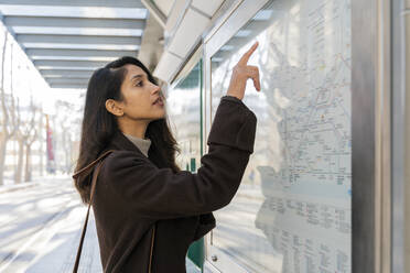 Junge Frau, die an der Straßenbahnhaltestelle eine Karte betrachtet - AFVF05304