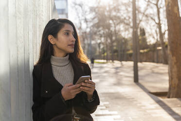 Junge Frau mit Smartphone in der Stadt, die sich umschaut - AFVF05309