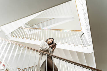 Junge Frau mit Smartphone geht die Treppe im Treppenhaus hinunter - AFVF05327
