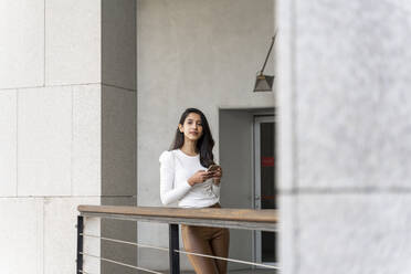 Young woman holding smartphone on balcony - AFVF05358