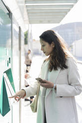 Junge Frau benutzt Fahrkartenautomat an der Straßenbahnhaltestelle - AFVF05366