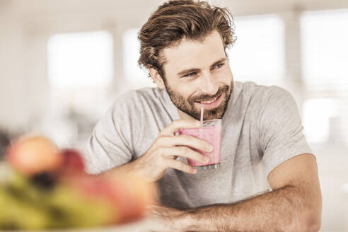 Young man smiling and drinking a fruit smoothie - SDAHF00156