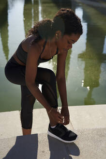 Spain, Catalonia, Barcelona, Young woman looking down as she ties her shoelace - PACF00185