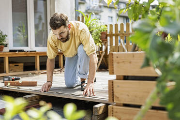 Junger Handwerker beim Bau einer Holzterrasse vor seinem Haus - PESF01765