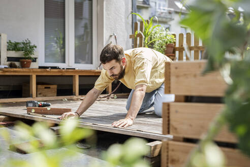 Junger Handwerker beim Bau einer Holzterrasse vor seinem Haus - PESF01766