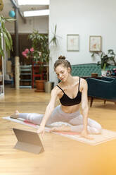 Young woman practicing yoga at home, using yoga app on digital tablet - PESF01775