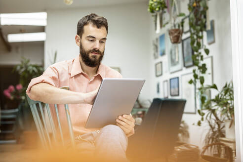 Young man sitting in living room, using digital tablet - PESF01782