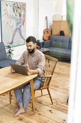 Young man sitting in living room, using digital tablet - PESF01789