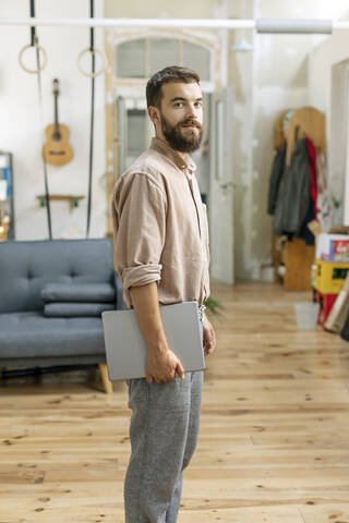 Selbstbewusster junger Mann, der zu Hause steht und ein digitales Tablet trägt, lizenzfreies Stockfoto