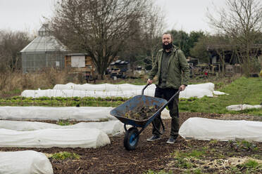 Man working in vegetable nursery, pushing wheelbarrow - FLLF00404