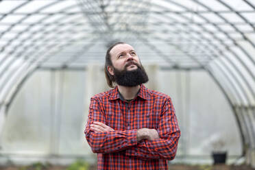 Confident man standing in greenhouse with arms crossed - FLLF00412