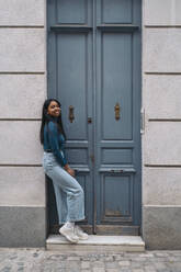 Portrait of smiling young woman standing at a door in the city - MPPF00509