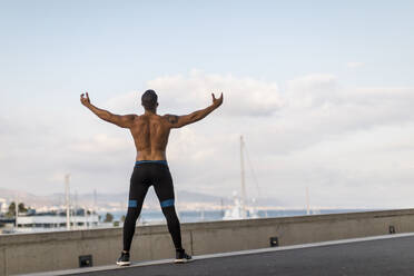 Rückansicht eines Joggers, der beim Training am Hafen die Arme hebt, Barcelona, Spanien - MAUF03342