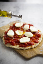 Olivenöl auf eine halbfertige Margharita-Pizza gießen - GIOF07978